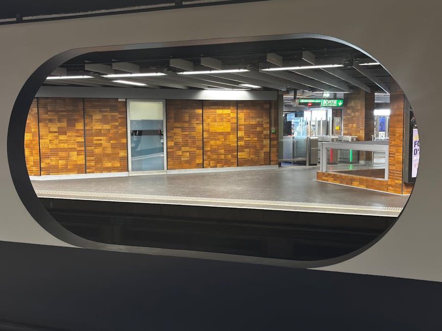 View of Uxbridge station platform as seen through a train window, featuring wooden wall panels, a metal turnstile gate, and glass doors. The platform surface appears clean with a smooth, grey finish.